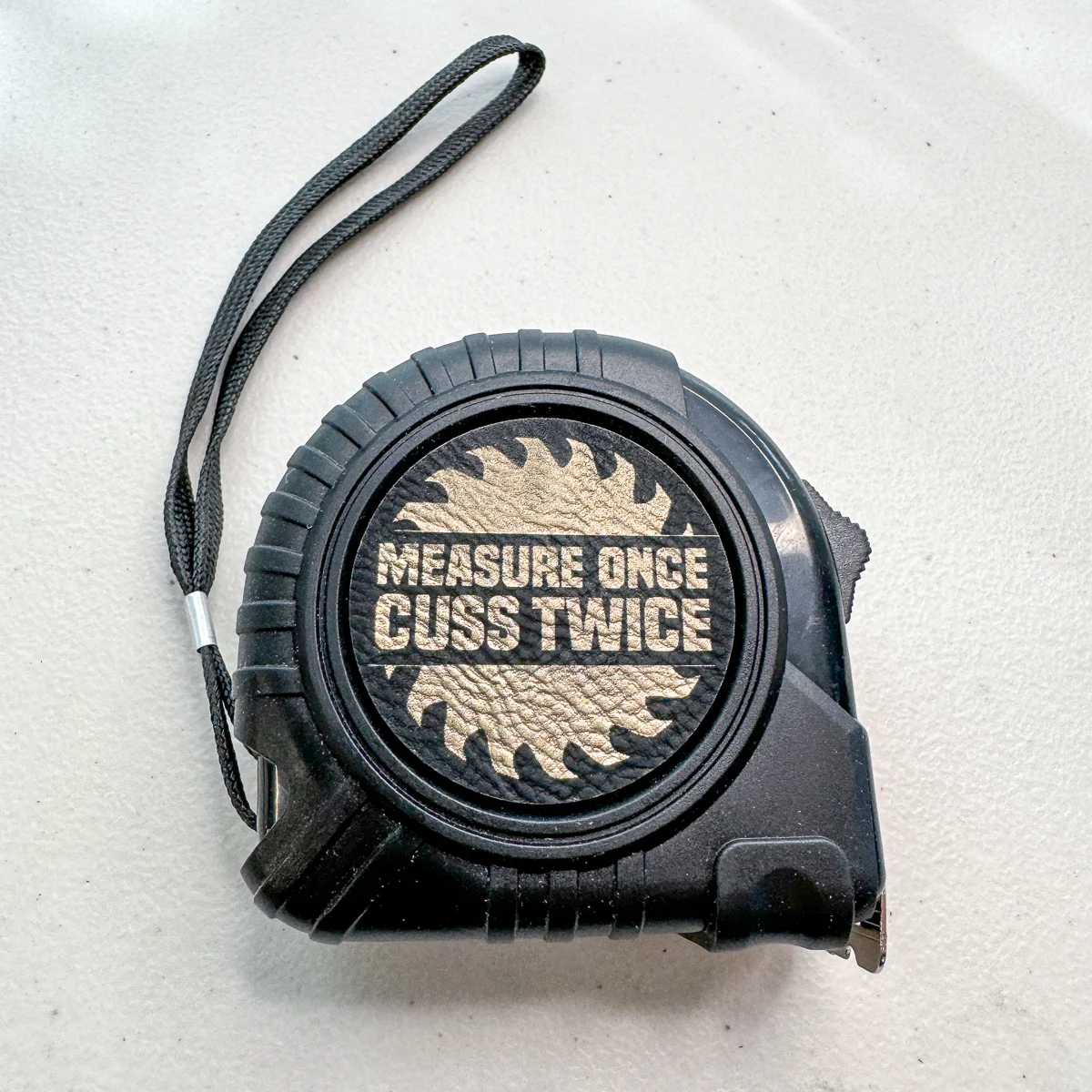 personalized tape measure with black leatherette patch engraved in gold that says "Measure Once Cuss Twice"