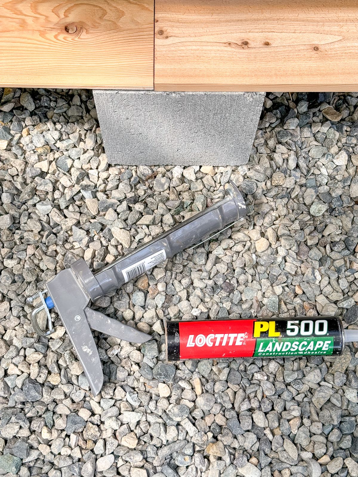 landscape adhesive and caulk gun on gravel in front of cinder block shelves